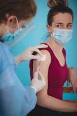 woman looks worried and horrified at a doctor injecting her with a vaccine against Covid-19....