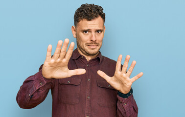 Young hispanic man wearing casual clothes afraid and terrified with fear expression stop gesture with hands, shouting in shock. panic concept.