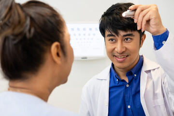 Fototapeta premium Selective focus at Optometrist face. While doctor using penlight and subjective refraction to examine eye visual system of elder patient women with professional machine before made glasses.