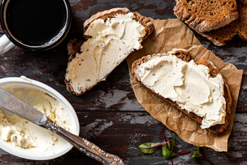 Rustic breakfast. Sandwich with soft cheese and rye bread on a dark wooden background top view. Ricotta sandwich and coffee.