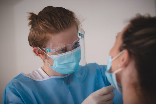 Doctor In A Sterile And Protective Suit Takes A Sample To Assess Positivity At The Collection Center. Swab From The Patient's Nose. Girl In A Red T-shirt On A Coronavirus Test