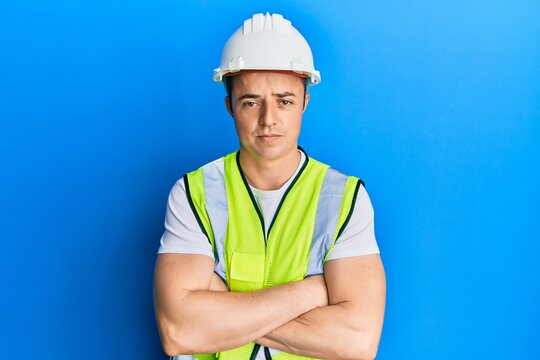 Handsome young man wearing safety helmet and reflective jacket skeptic and nervous, disapproving expression on face with crossed arms. negative person.