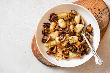 Gnocchi with mushrooms. Cooked potato gnocchi with fried champignons and onions in a white plate on a light concrete table top view. Italian cuisine. Copy space for text.
