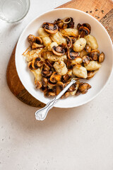 Gnocchi with mushrooms. Cooked potato gnocchi with fried champignons and onions in a white plate on a light concrete table top view. Italian cuisine. Copy space for text.