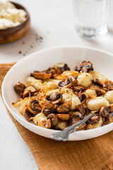 Gnocchi with mushrooms close-up. Cooked potato gnocchi with fried champignons and onions in a white plate on a light concrete table. Italian cuisine.