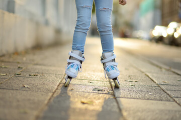 Young girl learning to roller skate on beautiful summer day on a street.