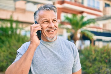 Middle age hispanic grey-haired man smiling happy talking on the smartphone at the park.