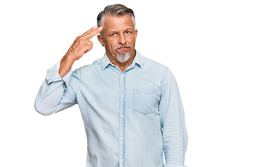 Middle age grey-haired man wearing casual clothes shooting and killing oneself pointing hand and fingers to head like gun, suicide gesture.