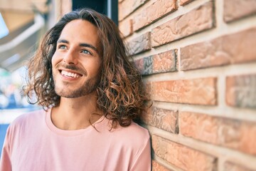 Young hispanic man smiling happy looking to the side leaning on the wall