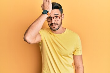 Young hispanic man wearing casual clothes and glasses surprised with hand on head for mistake,...