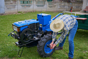 A man replaces the wheels,the farmer tightens the bolts on the wheel of a two-wheeled tractor in the yard