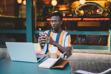Millennial IT professional in glasses checking received notification on modern cellphone device...
