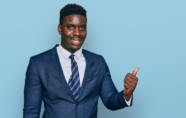 Handsome business black man wearing business suit and tie smiling with happy face looking and pointing to the side with thumb up.