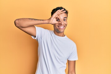 Fototapeta na wymiar Young handsome african american man wearing casual white tshirt smiling happy doing ok sign with hand on eye looking through fingers