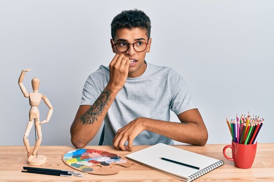 Young handsome african american man painter sitting palette and art manikin looking stressed and nervous with hands on mouth biting nails. anxiety problem.