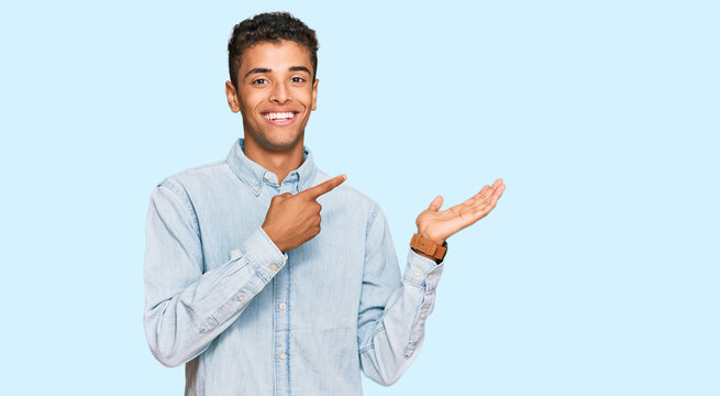 Young handsome african american man wearing casual clothes amazed and smiling to the camera while presenting with hand and pointing with finger.