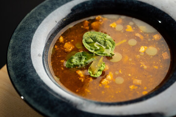 Hot soup with smoked meats in a dark blue plate on a black background close-up.