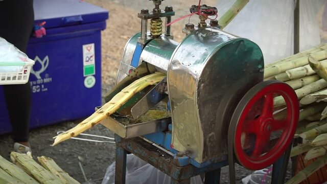 Street vendor in Thailand  extracting sugarcane juice from sugarcanes using a squeezer machine.