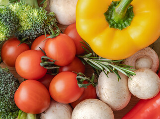 Top view of fresh cherry tomatoes, yellow pepper, mushrooms and broccoli on the table. Mixed vegetables.