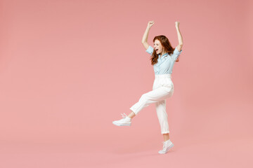 Fototapeta na wymiar Full length body young student successful overjoyed excited happy redhead woman 20s in blue shirt pants walk do winner gesture clench fist celebrate isolated on pastel pink background studio portrait.