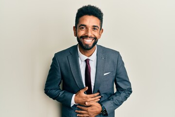 Handsome hispanic man with beard wearing business suit and tie smiling and laughing hard out loud because funny crazy joke with hands on body.