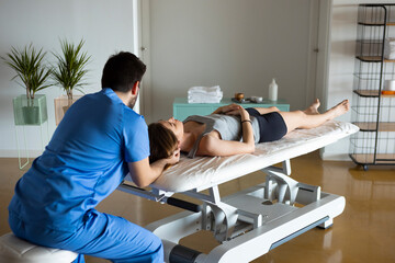 Rear view of a professional masseur in blue uniform, holding woman's head, who is lying down on a...
