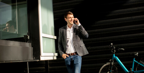 Young businessman walking away from the ebike and using mobile phone