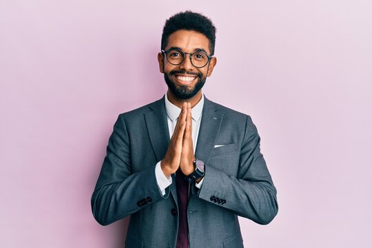 Handsome hispanic business man with beard wearing business suit and tie praying with hands together asking for forgiveness smiling confident.