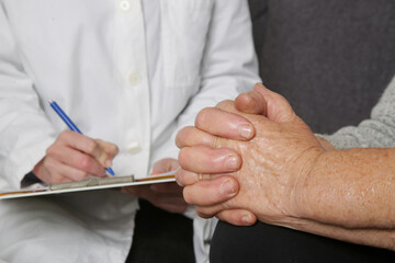 Senior woman visiting doctor. Close up image of elderly patient and doctor taking notes.