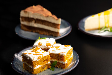 A few different desserts, assorted sweets on plates on a black background. Vanilla classic and chocolate cake, carrot cake.