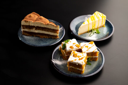 A few different desserts, assorted sweets on plates on a black background. Vanilla classic and chocolate cake, carrot cake.