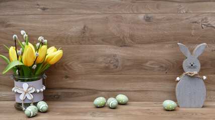 Gelbe Tulpen mit Osterhase und Ostereiern vor einem Holzhintergrund.