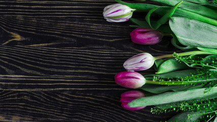 flatley flower arrangement of pink and white tulips with green leaves on a dark wooden background kopi space