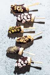 Flat lay of bananas in dark chocolate with healthy toppings on stick, gray background. Healthy vegan dessert concept.