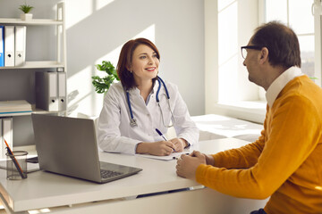 Friendly smiling caucasian woman doctor listening senior adult man complaints making notes in patient card clipboard or healthcare insurance form at initial medical consultation appointment
