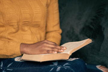 black woman reading a book on a couch, focus on hand