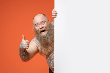 Fat obesy pudge chubby overweight tattooed bearded man with naked torso hold white empty blank...