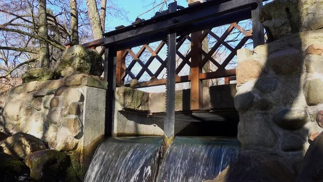 Water Lock Gate Control Gears with Cogwheels On Canal with Waterfall and Rocky Stream underneath on Bright Sunny Morning
