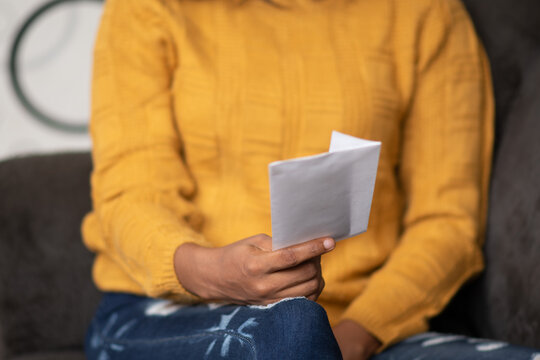 Beautiful Young Black Woman Holding A Letter Envelope, Sitting On A Couch