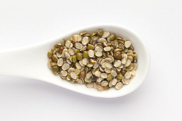 macro Close-up of Organic green Gram (Vigna radiata) or spilt green moong dal unpolished on a white ceramic soup spoon. Top view