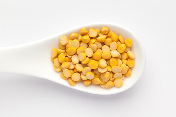 Macro Close-up of Organic Bengal Gram (Cicer arietinum) or split yellow chana dal on a white ceramic soup spoon. Top view