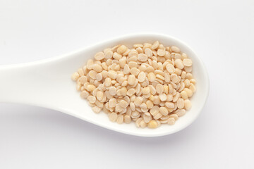 macro Close-up of Organic split polished white urad dal (Vigna mungo) on a white ceramic soup spoon. Top view