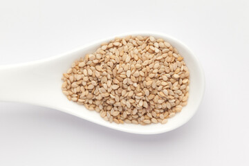 Macro Close up of Organic White Sesame seeds(Sesamum indicum) or white Til with shell on a white ceramic soup spoon. Top view