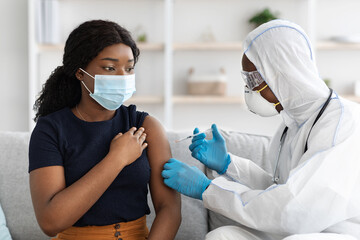Black woman in face mask getting injection at home