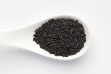 Macro Close up of Organic Black Sesame seeds(Sesamum indicum) or Black Til with the shell on a white ceramic soup spoon. Top view
