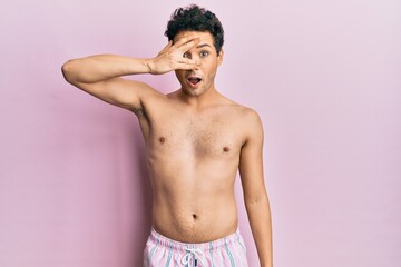 Fototapeta premium Young handsome man wearing swimwear shirtless peeking in shock covering face and eyes with hand, looking through fingers with embarrassed expression.
