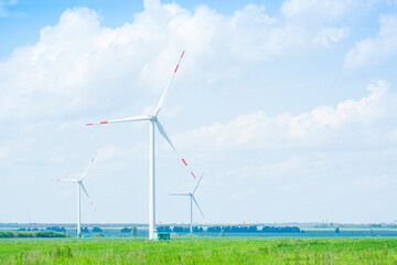 many windmills stand on a large field spinning in the day against a sunset orange sky. Alternative Energy Concept