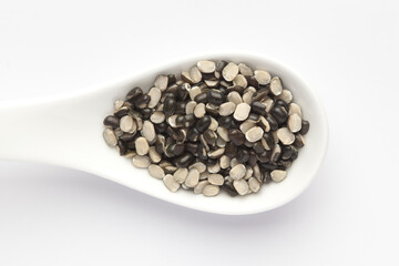 Macro Close up of Organic split black urad dal (Vigna mungo) with shell on a white ceramic soup spoon. Top view