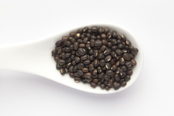 Macro Close-up of Organic Black Gram (Vigna mungo) or whole black urad on a white ceramic soup spoon. Top view