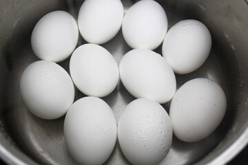 The process of boiling white eggs in a stainless saucepan of bubbling water on black background. The preparation for painting of eggs before Easter Holiday.